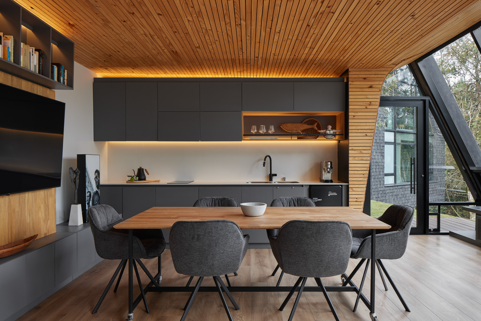 Comedor con techo en listones de madera y cocina en gris mate